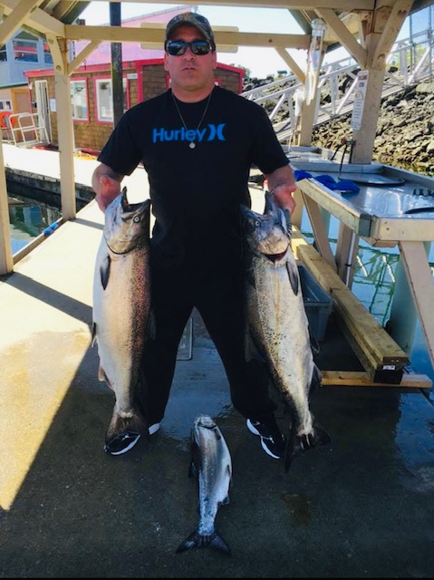 Douglas with three at a fish cleaning station on a dock. He is holding two of the fish, presenting them to the camera.